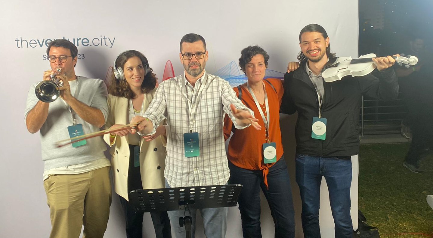 The TheVentureCity data team miming a rock band: trumpet, violin, conductor and headphones, in front of the company backdrop.