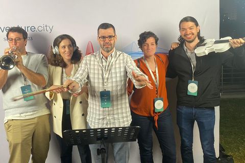 The TheVentureCity data team miming a rock band: trumpet, violin, conductor and headphones, in front of the company backdrop.